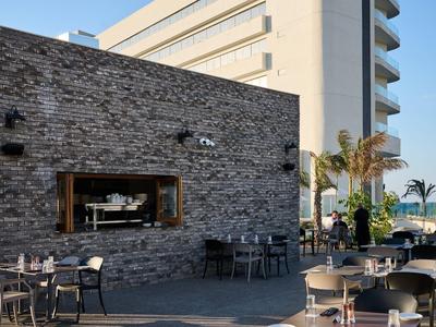 Area esterna moderna di un hotel con tavoli, sedie e vista sul mare con cielo sereno.