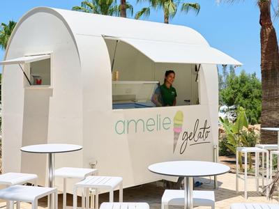 Chiosco bianco moderno con scritta 'amelie fruits' in un ambiente esterno mediterraneo soleggiato.