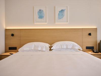 Camera d'hotel moderna con letto matrimoniale, testiera in legno, comodini e decorazioni minimaliste.