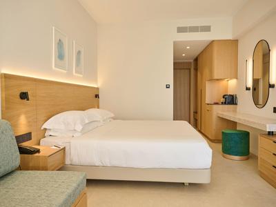 Camera d'hotel luminosa con letto matrimoniale, dettagli in legno, zona salotto e bagno moderno.