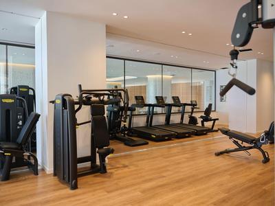 Palestra moderna in hotel con tapis roulant, macchine per la forza e pavimenti in legno chiaro.