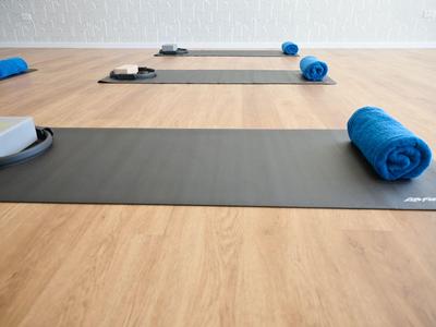 Tre tappetini da yoga con asciugamani blu e blocchi grigi su un pavimento in legno chiaro in una stanza.