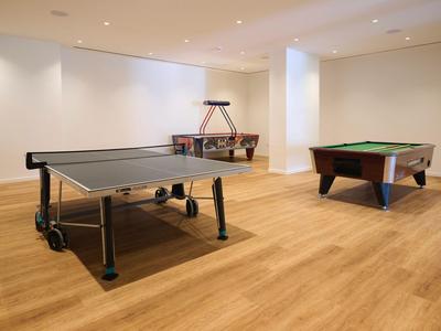 Sala giochi moderna con tavolo da ping pong, calcio balilla e tavolo da biliardo su pavimento in legno chiaro.