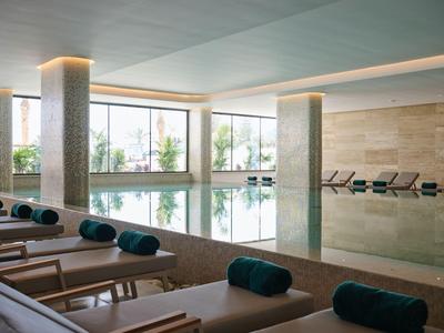 Piscina coperta luminosa con lettini e grandi finestre che offrono luce naturale e vista esterna.