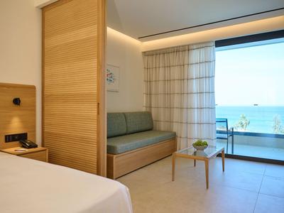 Camera d'hotel con parete divisoria in legno, divano, tavolo e vista mare attraverso una parete in vetro.