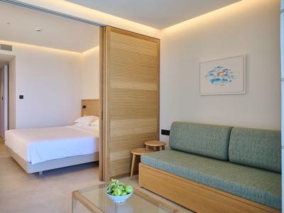 Camera d'hotel luminosa con letto matrimoniale, divano, mobili in legno e arredamento minimalista.