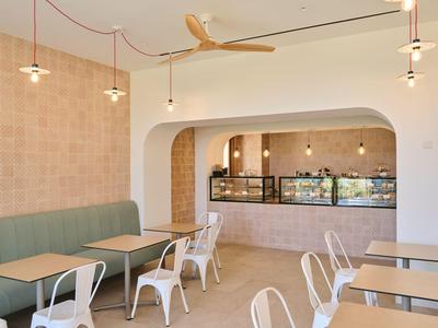 Caffè moderno con arredamento minimalista, sedie bianche e tavoli in legno accanto a un bancone.