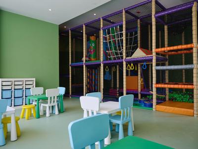 Spazio interno con struttura per arrampicata colorata e diversi piccoli tavoli e sedie per bambini.