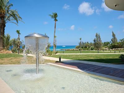 Fontana moderna con cappello in metallo nel giardino dell'hotel, palme e mare sullo sfondo.