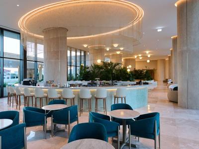 Ristorante moderno dell'hotel con bancone, sedie blu e grandi pilastri sotto illuminazione calda.
