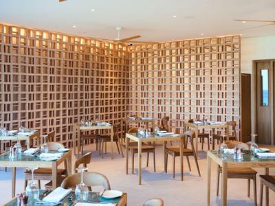 Sala da pranzo moderna con tavoli in legno e parete geometrica dai toni caldi.