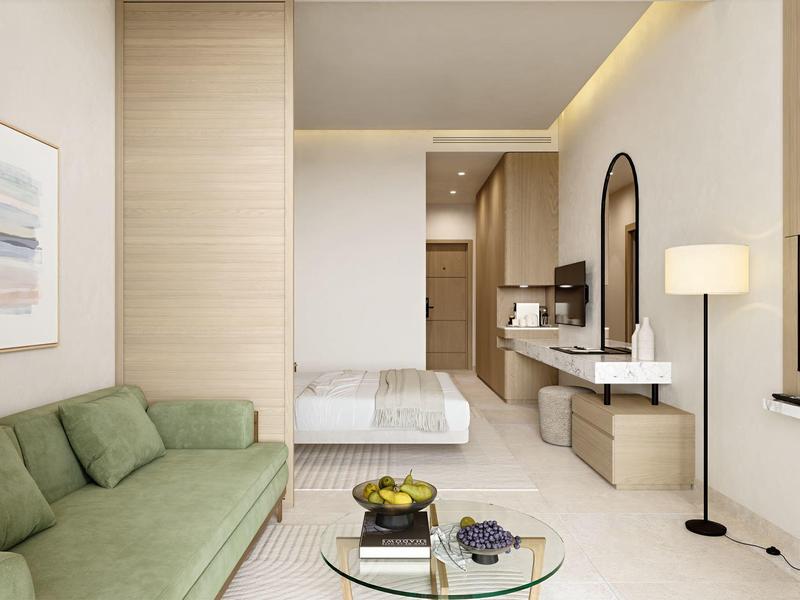 Modern hotelkamer met groene bank, glazen salontafel en comfortabel bed in neutrale tinten.