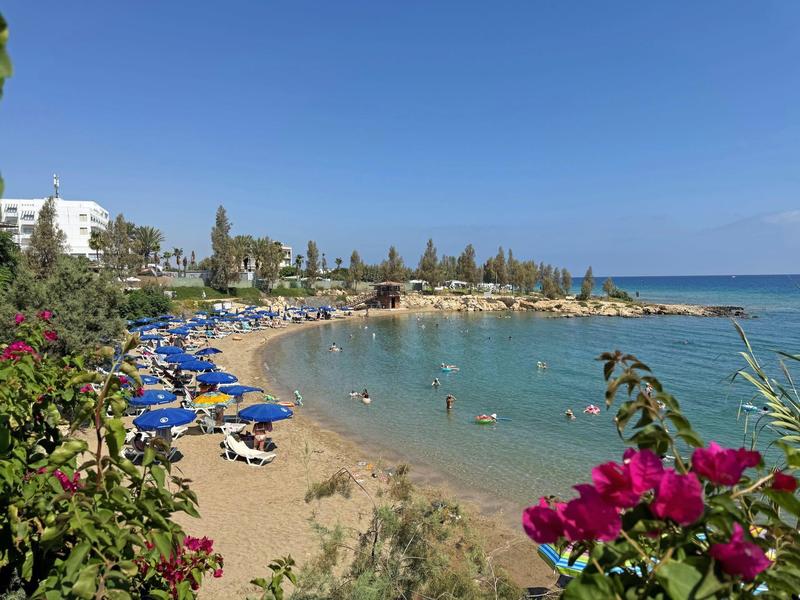 Zandstrand met blauwe ligstoelen en mensen in helder water onder een blauwe lucht