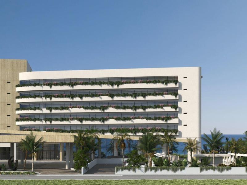 Modern hotelgebouw met meerdere balkons, omgeven door palmbomen en blauwe lucht.