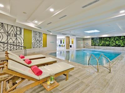 Innen-Schwimmbad mit Liegestühlen, grüner Wanddeko und hellem Holzfußboden.