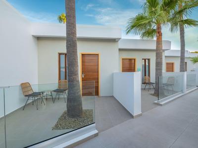 Moderne weiße Häuser mit Holztüren, Glasgeländern und Palmen in einem sonnigen Außenbereich.