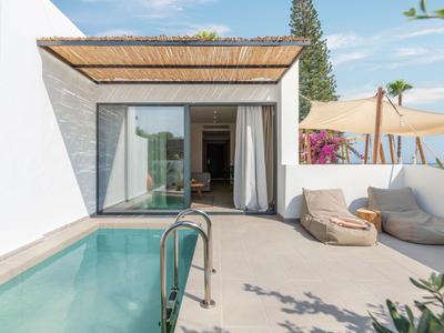 Moderner Garten mit kleinem Pool, weißer Mauer, Holzüberdachung und Sitzsäcken in heller Sonne.