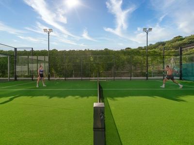 Dos personas juegan pádel en una cancha al aire libre bajo un cielo soleado.