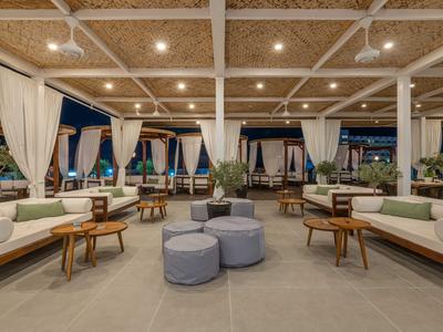 Área de lounge abierta con asientos modernos, mesas de madera y cortinas en un hotel.