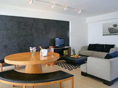 Modernes Wohnzimmer mit grauer Couch, rundem Holztisch, schwarzer Bank und dunkler Akzentwand.