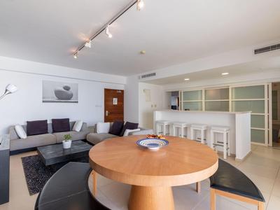 Moderne offene Wohnküche mit Holztisch, Barhockern, grauem Sofa und weißem minimalistischen Design.