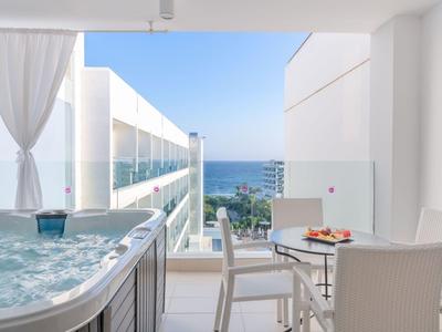 Moderner Balkon mit Whirlpool, Tisch, Stühlen und Meerblick unter blauem Himmel.