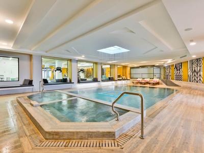 Heller Wellnessbereich mit Pool, Whirlpool, Holzdecke und gelben Wandakzenten.