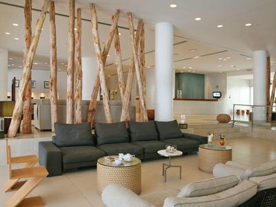 Moderner Wohnzimmerbereich mit grauem Sofa, Holzstämmen als Raumteiler und hellen Möbeln.