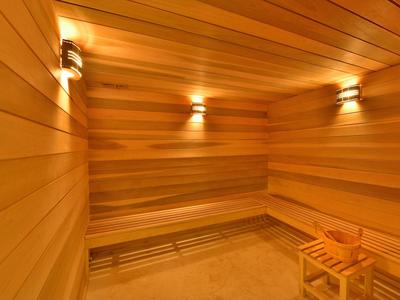 Innenraum einer Sauna aus hellem Holz mit Bänken und drei Wandlampen.
