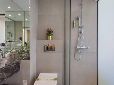 Moderne Badezimmerwand mit Toilette, Glas-Dusche und grauen Fliesen in schlichter Gestaltung.