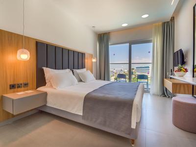 Modernes Schlafzimmer mit großem Bett, grauer Bettdecke, Holzakzenten und Balkonblick.