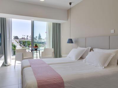 Habitación de hotel moderna con dos camas individuales, balcón y vista a palmeras y mar.