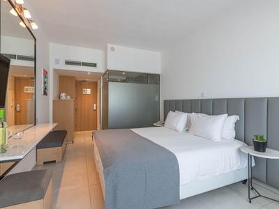 Moderner Hotelzimmer mit großem Bett, grauem Kopfteil, weißen Wänden und minimalistischer Einrichtung.