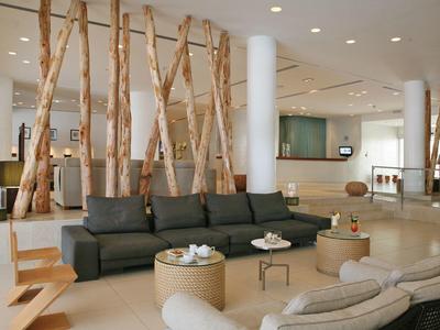 Moderner Wohnraum mit dunkelgrauem Sofa, hellen Sesseln, Holzstämmen und minimalistischer Dekoration.