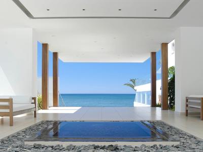 Offener, moderner Raum mit Meerblick, klaren Linien, Holzsäulen und Wasserbecken im Vordergrund.