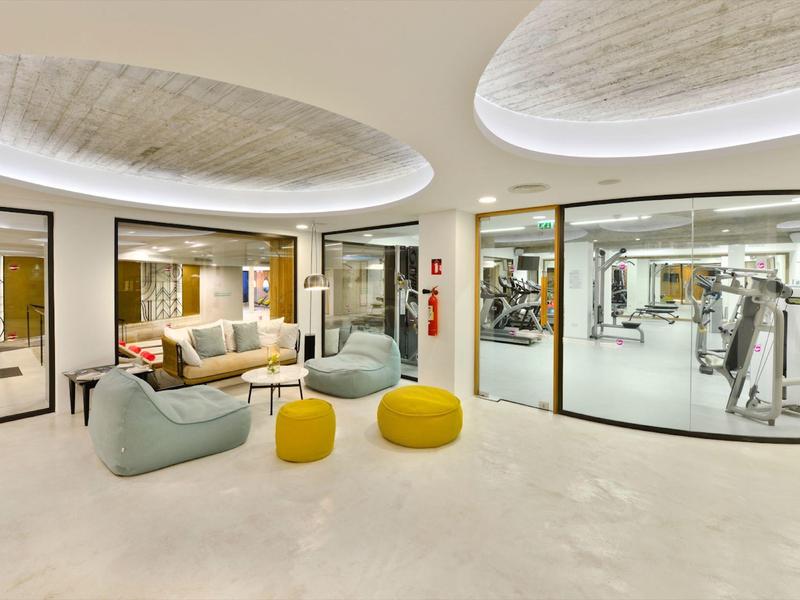 Heller Fitnessraum mit modernen Geräten, Sitzbereich und runden Deckenleuchten.