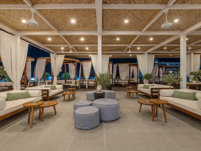 Großer, offener Lounge-Bereich mit weißen Sofas, hölzernen Tischen und Decke mit Naturmaterial.