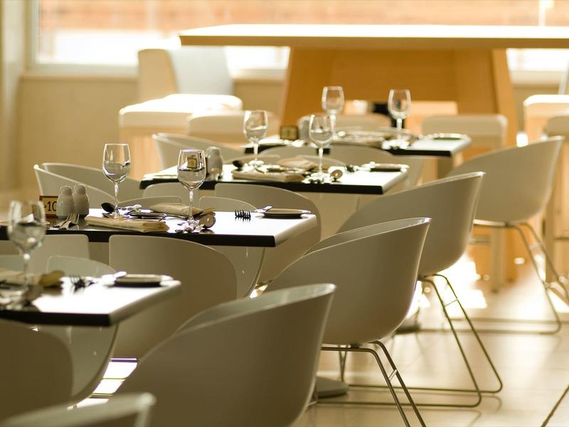 Hell eingerichteter Speisesaal mit weißen Stühlen und gedeckten Tischen bei Tageslicht.