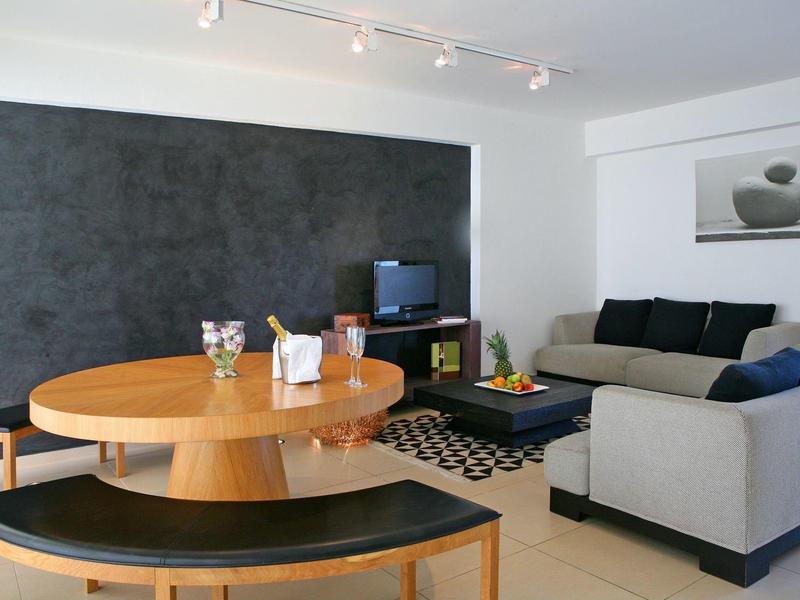 Modernes Wohnzimmer mit grauer Couch, rundem Holztisch, schwarzer Bank und dunkler Akzentwand.