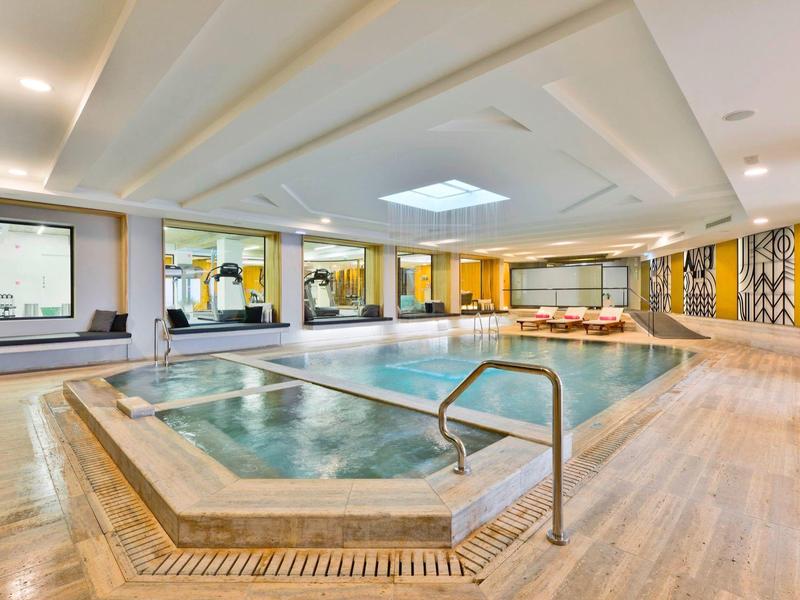 Heller Wellnessbereich mit Pool, Whirlpool, Holzdecke und gelben Wandakzenten.