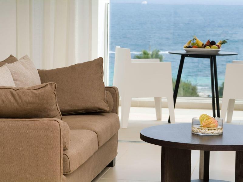 Wohnzimmer mit braunem Stoffsofa, rundem dunklem Tisch und Meerblick durch große Fenster.