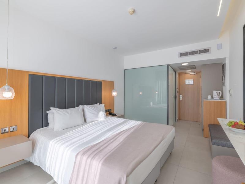 Modernes Hotelzimmer mit großem Bett, grauen Akzenten und hellem Holzmöbeln, heller Raumgestaltung.