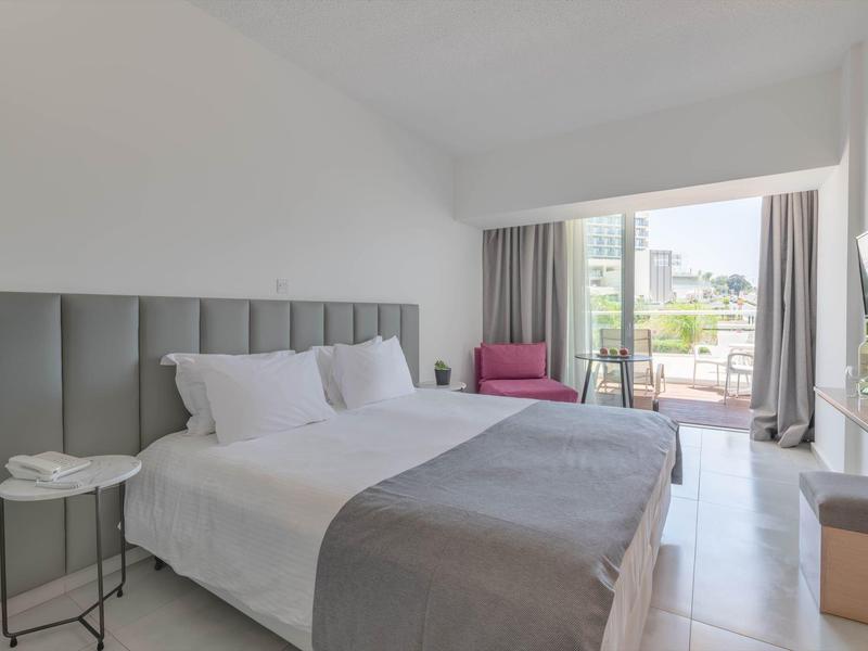 Helles Schlafzimmer mit großem Bett, grauem Kopfteil, weißer Bettwäsche und Zugang zum Balkon.