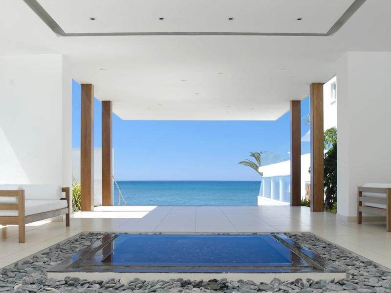 Offener, moderner Raum mit Meerblick, klaren Linien, Holzsäulen und Wasserbecken im Vordergrund.