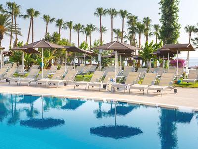 Zwembad met ligstoelen en parasols, omgeven door palmbomen en grasveld