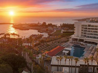 Hotel mit großem Pool nahe Küste bei Sonnenuntergang mit orangefarbenem Himmel.