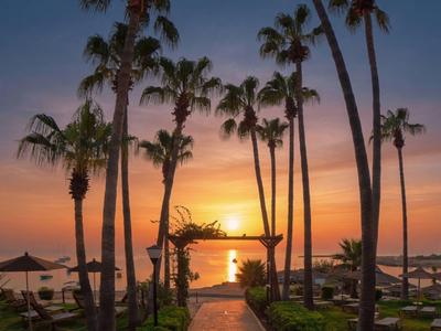 Ein tropischer Hotelgarten mit Palmen und Sonnenuntergang über dem Meer.