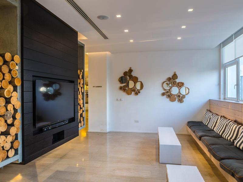 Chambre d'hôtel moderne avec mur télé, décor en bois et longue banquette avec coussins.