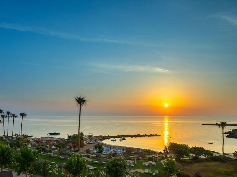 Coucher de soleil sur une ville côtière avec des palmiers et une mer calme.