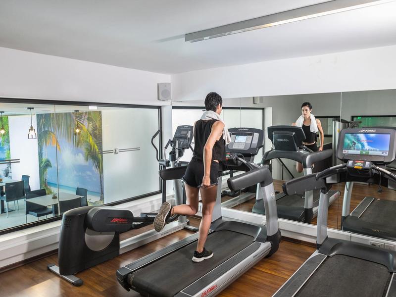 Femme s'entraînant sur un tapis roulant dans une salle de sport moderne avec miroirs.